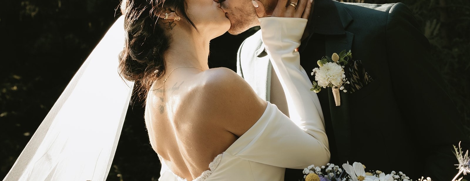 Married couple kissing, holding bouquet with veil flowing